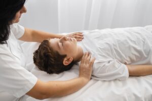 Un enfant allongé sur une table de massage recevant un soin relaxant par une praticienne, favorisant détente et concentration.